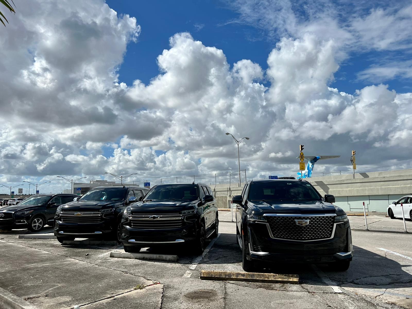 Black luxury SUVs at the airport, including the Luxury Rides Miami Cadillac Escalade