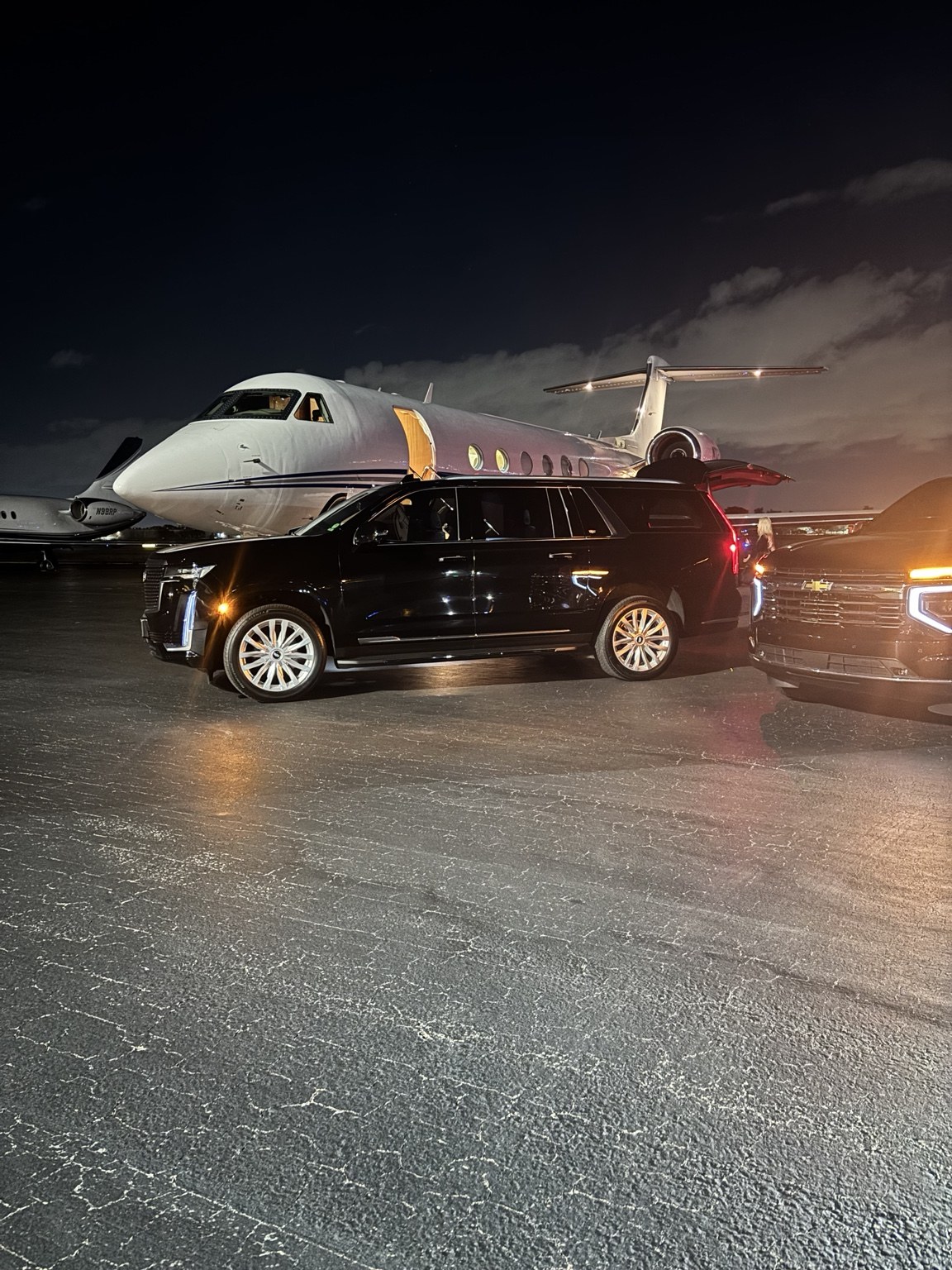 Black Cadillac Escalade beside a private jet at night