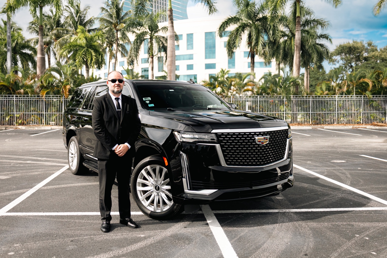 Luxury Rides Miami chauffeur standing beside the front of the black Cadillac Escalade ESV